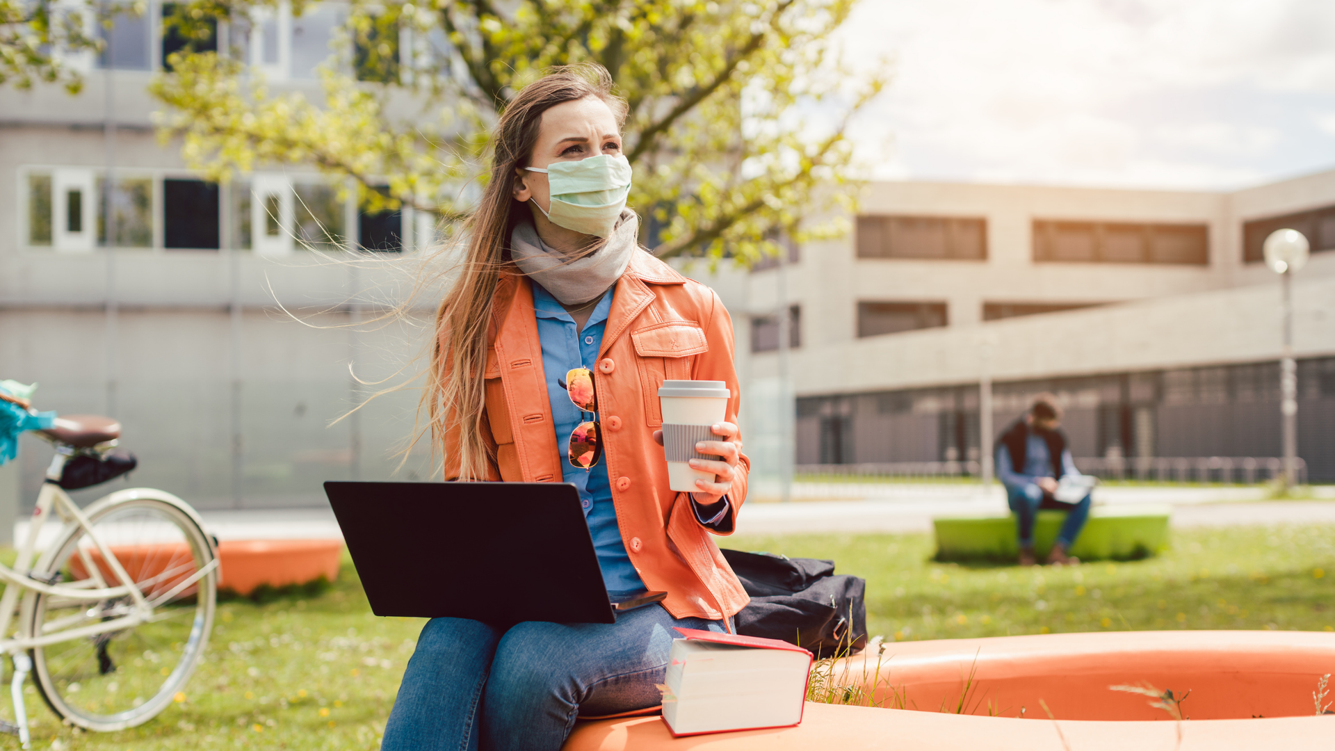 Remote student wearing a mask, holding coffee and looking at an employer brand on her laptop..